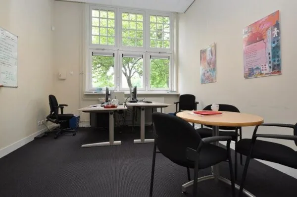 Kantoorruimte aan de Spechtlaan met twee bureaus, vergadertafel en grote ramen met uitzicht op groen.