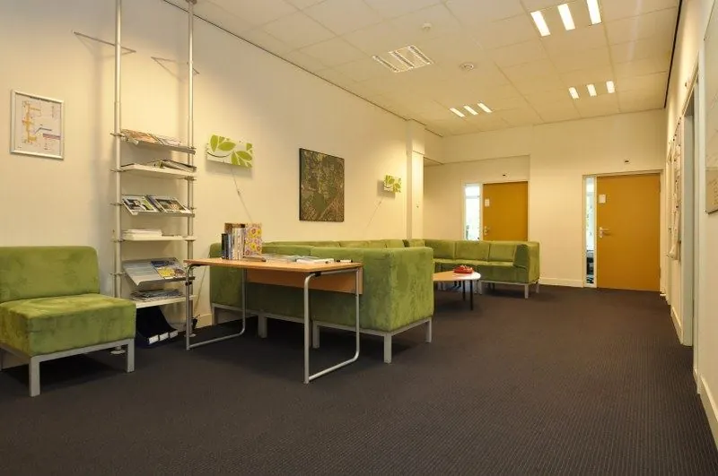 Wachtkamer met groene zitbanken, een leestafel en folders aan de muur in een kantoor aan de Spechtlaan.
