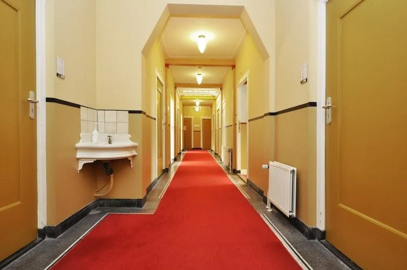 Verlichte gang in een gebouw aan de Spechtlaan met gele deuren, rood tapijt en een wandfontein.