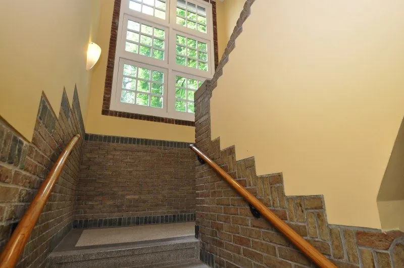 Trappenhuis met gele muren, bakstenen lambrisering en een groot raam aan de Spechtlaan.