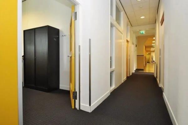 Verlichte gang in een kantoorpand aan de Spechtlaan met geopende deur naar een kamer met een zwarte kast.