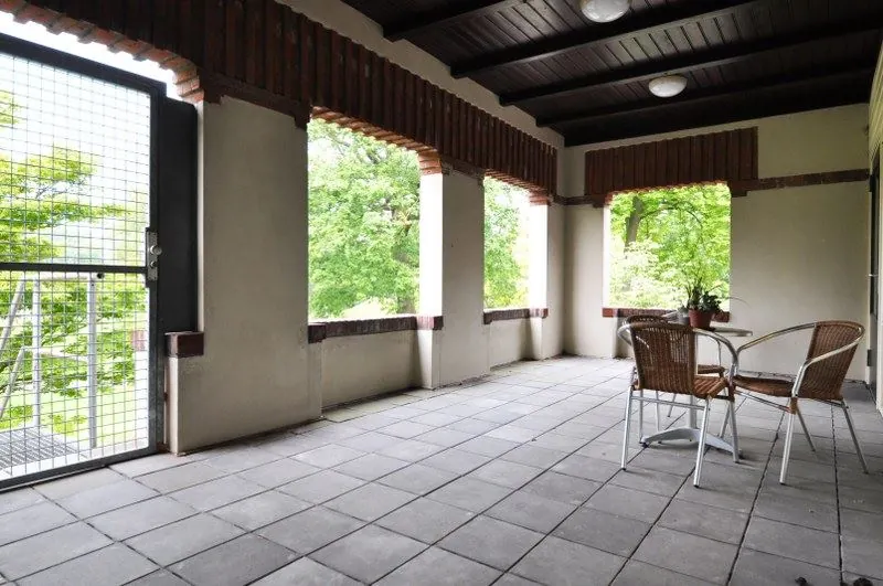 Overdekt balkon aan de Spechtlaan met betegelde vloer, houten plafond en zitje met uitzicht op groen.
