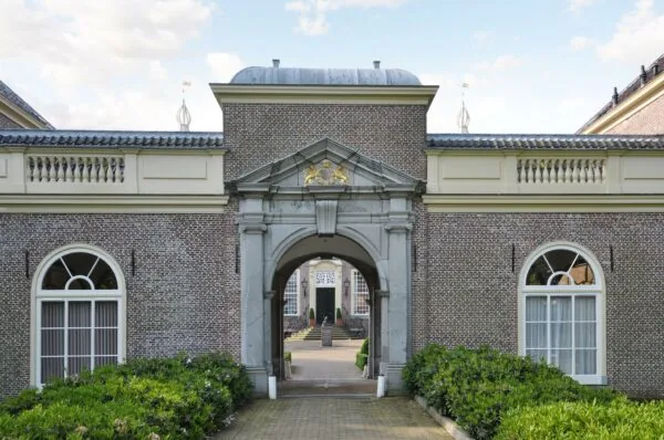 Toegangspoort van een historisch kasteelgebouw aan de Kasteellaan, met goudkleurig wapenschild boven de boog en zicht op de binnenplaats.