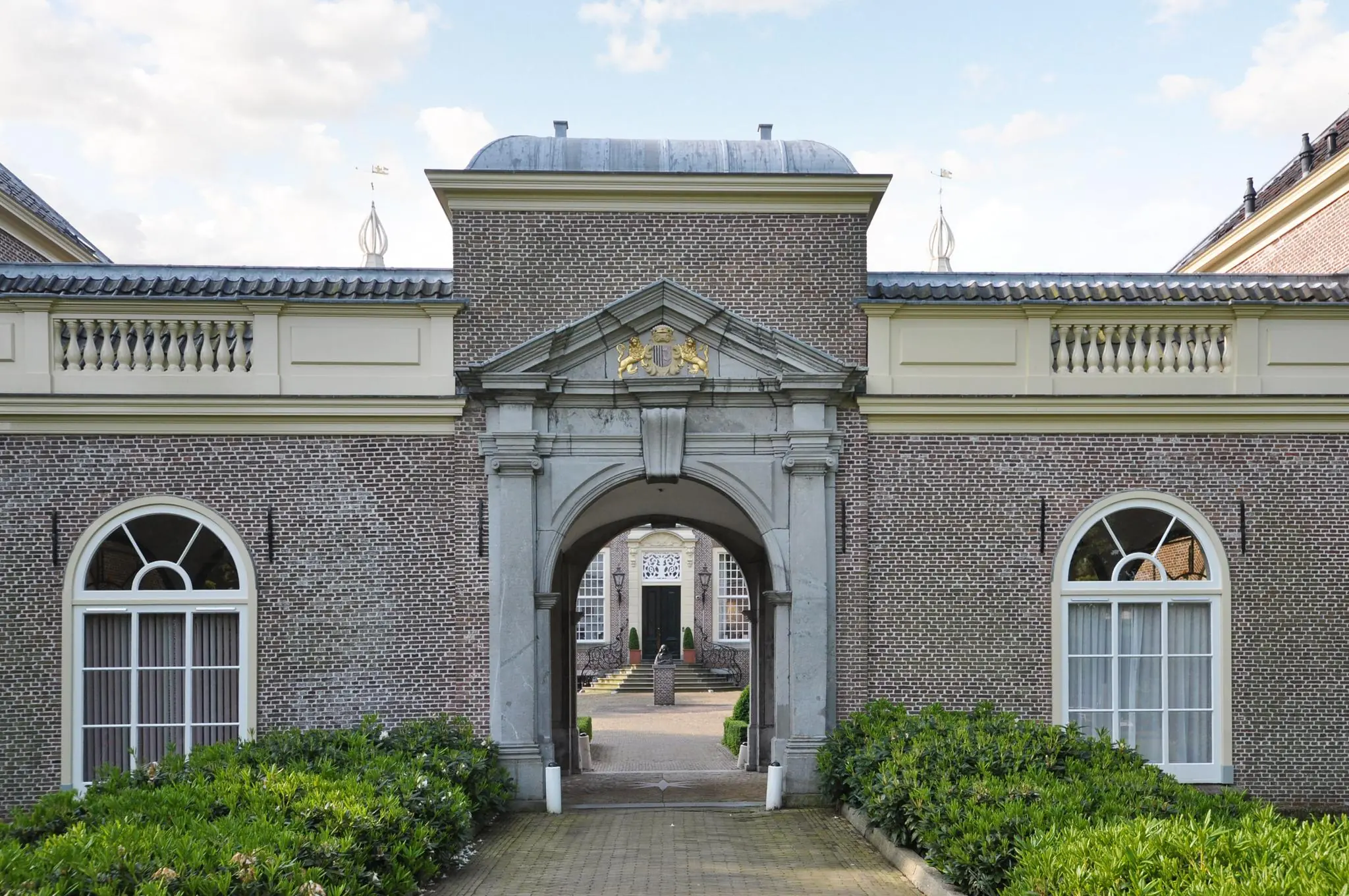 Toegangspoort van een historisch kasteelgebouw aan de Kasteellaan, met goudkleurig wapenschild boven de boog en zicht op de binnenplaats.