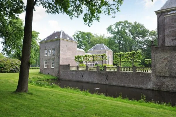 Bakstenen kasteelgebouw aan de Kasteellaan met gracht, groene tuin en omringende bomen.