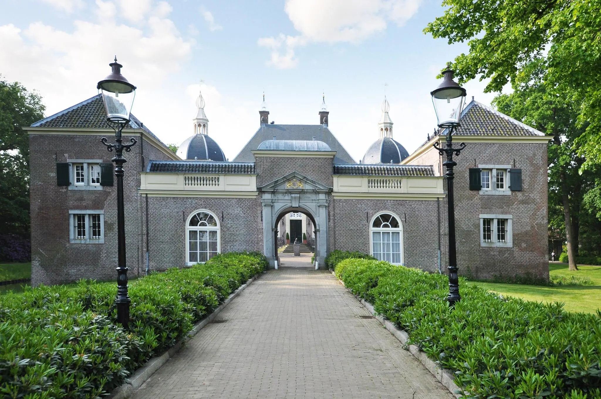 Toegangspoort en voorgevel van een historisch kasteel aan de Kasteellaan, omringd door groen en klassieke lantaarnpalen.