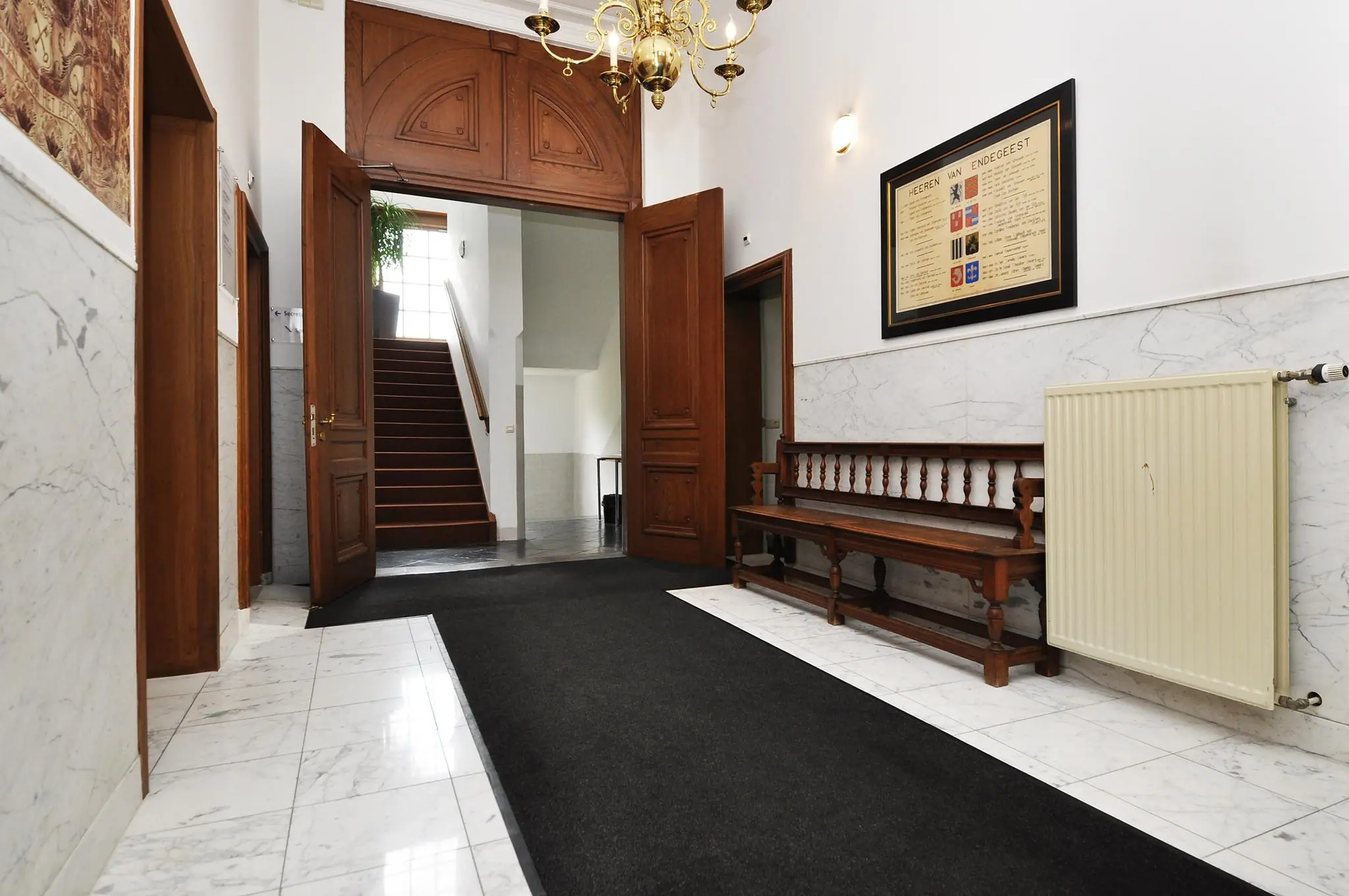 Ingangshal van een klassiek gebouw aan de Kasteellaan met marmeren vloer, houten deuren, trap en antieke houten bank.