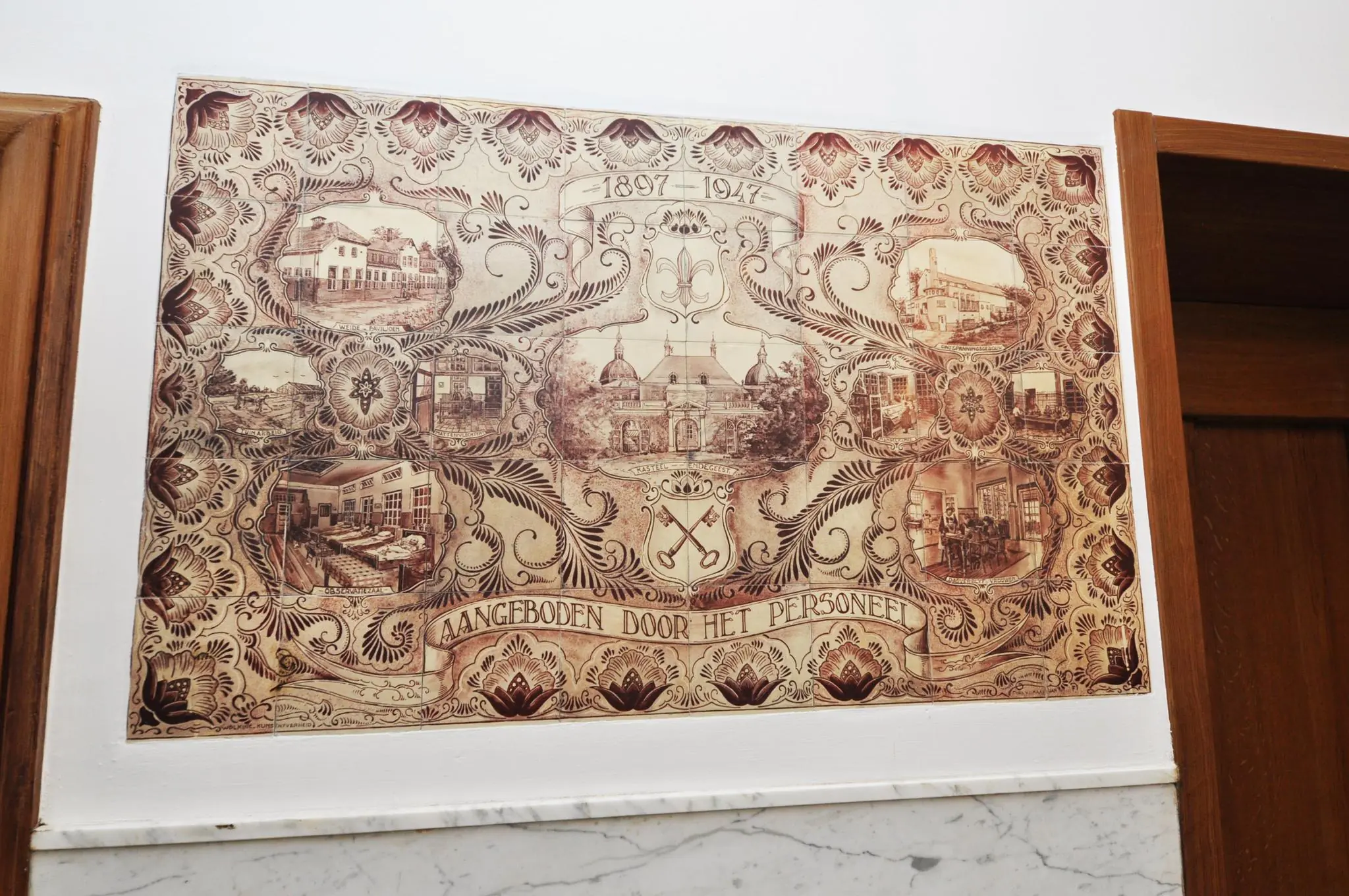 Decoratieve muurtegel met historische afbeeldingen van Kasteel Laerhof en omliggende gebouwen ter ere van het 50-jarig jubileum (1897–1947), aangeboden door het personeel.