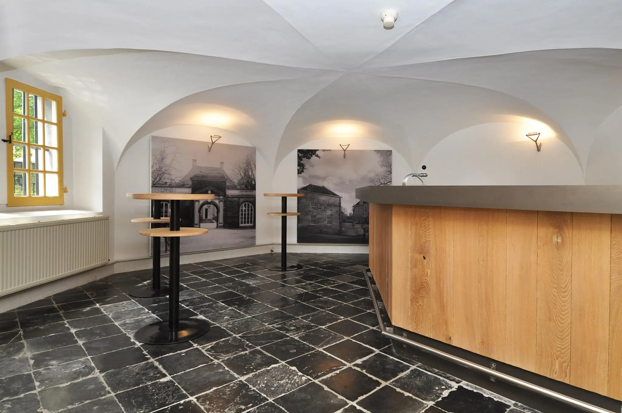 Moderne ontvangstruimte met houten bar, hoge tafels en zwart-wit foto's van Kasteellaan aan de muur.