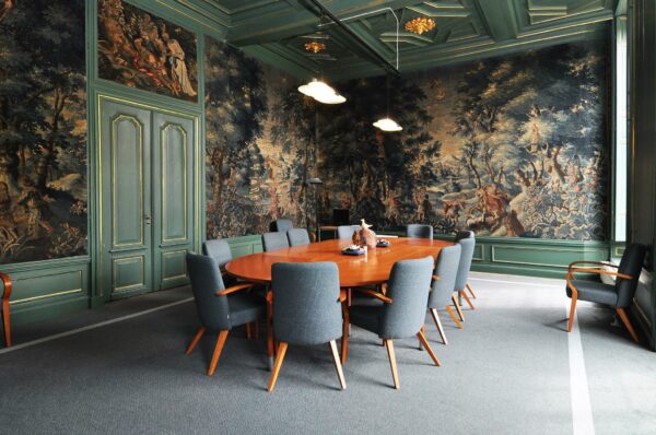 Vergaderruimte in Kasteellaan met houten tafel, stijlvolle stoelen en wandvullende wandtapijten met klassieke taferelen.