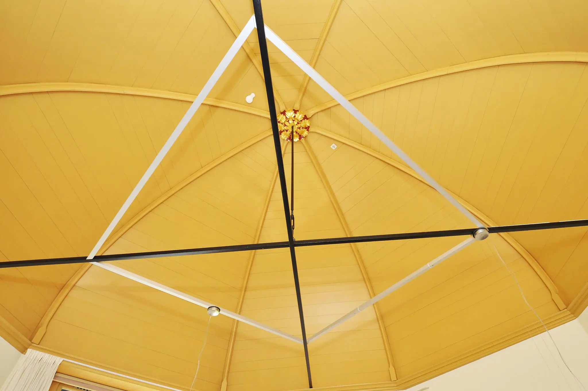 Gele, houten gewelfde plafondconstructie met sierlijke details en moderne verlichtingsbalken in Kasteellaan.