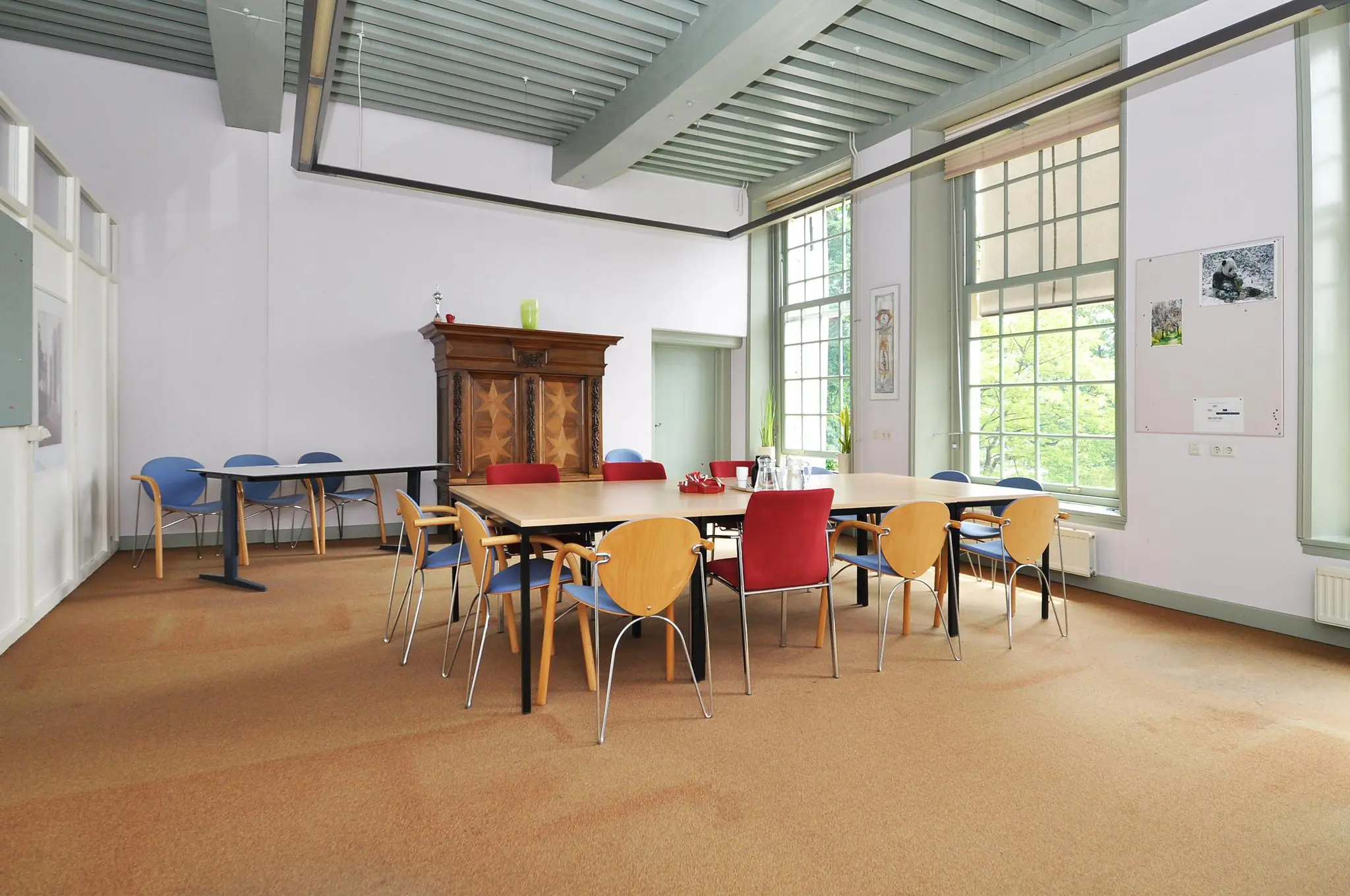 Vergaderruimte aan de Kasteellaan met een grote tafel, diverse stoelen en hoge ramen die uitzicht bieden op groen.