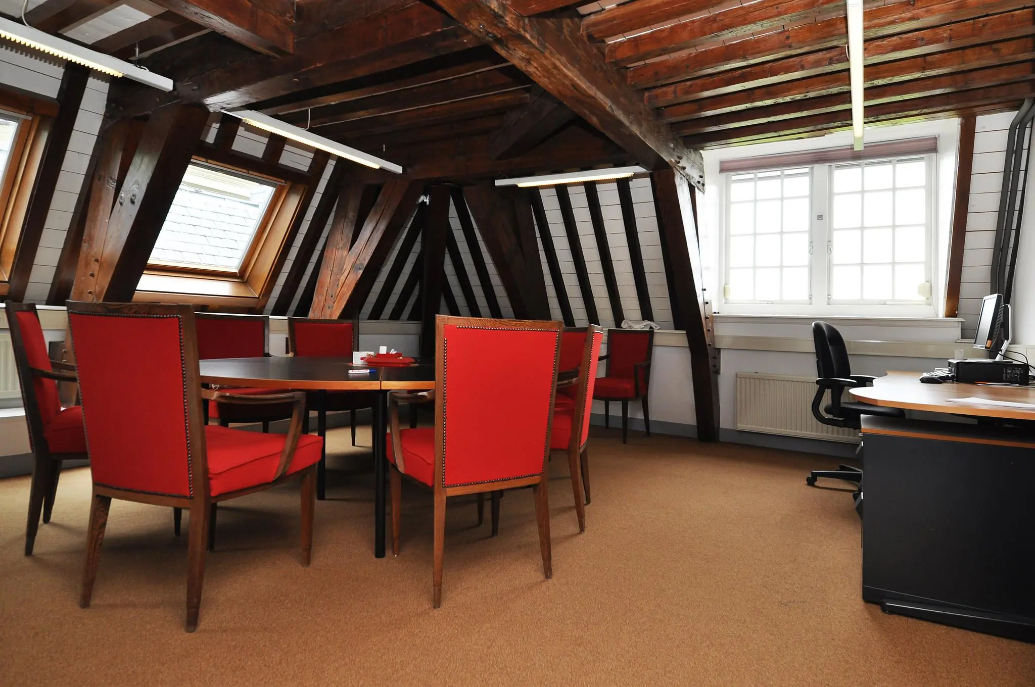 Vergaderruimte in een historisch pand met houten balken, rode stoelen en een bureau bij het raam aan de Kasteellaan.
