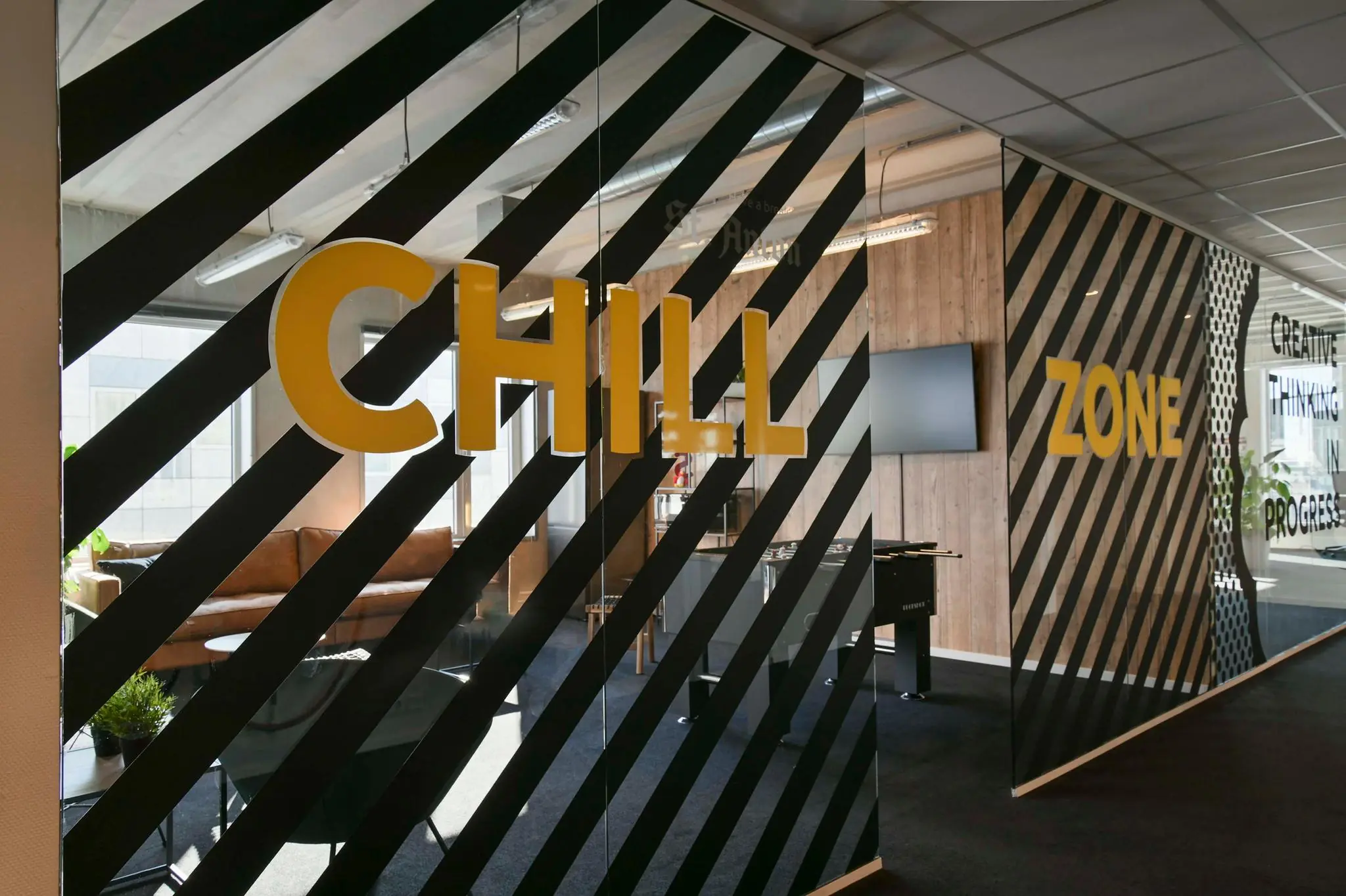 Moderne kantoorruimte met een glazen muur waarop in grote gele letters "CHILL ZONE" staat.