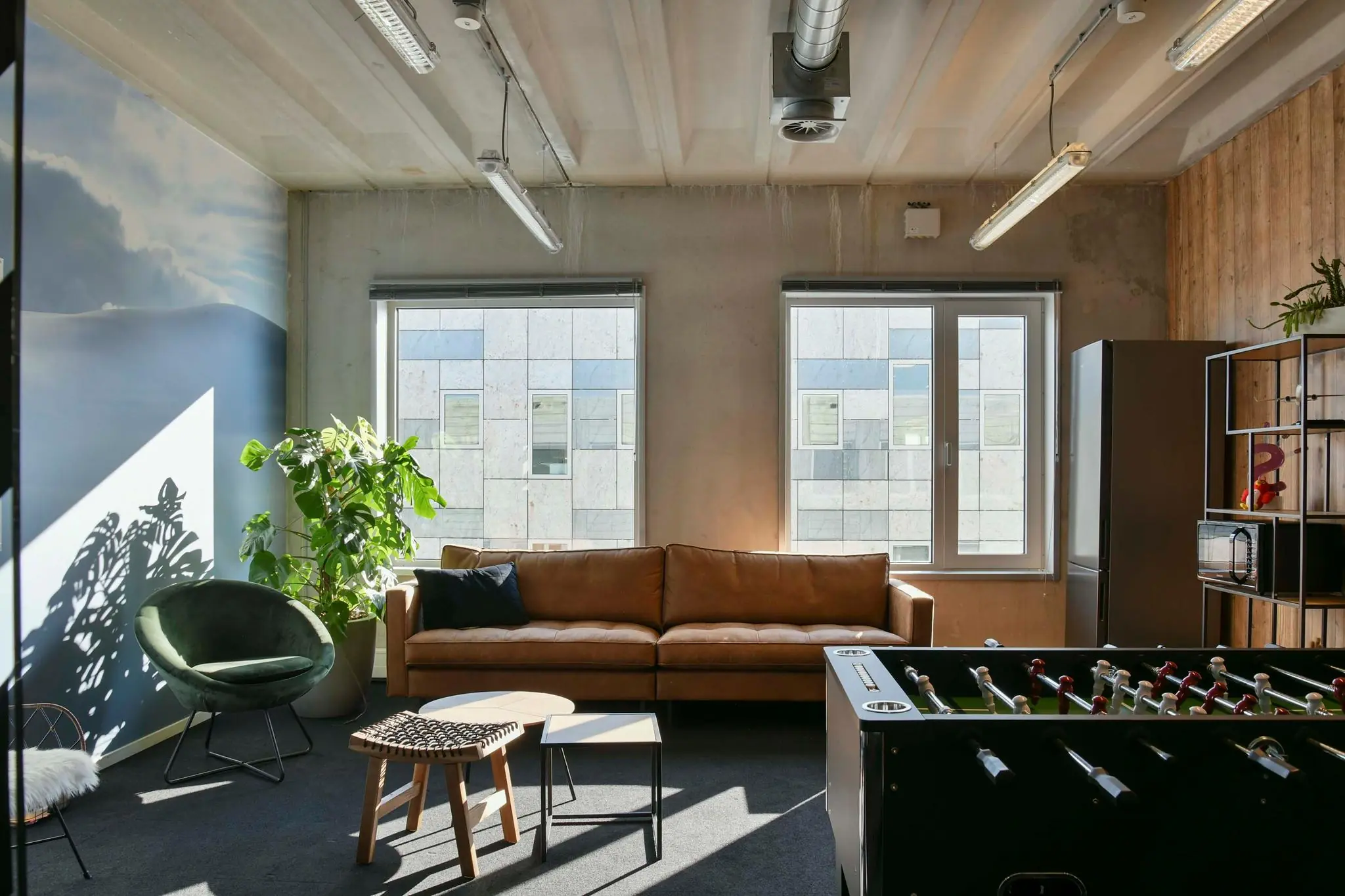 Moderne loungehoek in een kantoor aan de Bahialaan met een leren bank, foosbaltafel en grote kamerplant bij het raam.