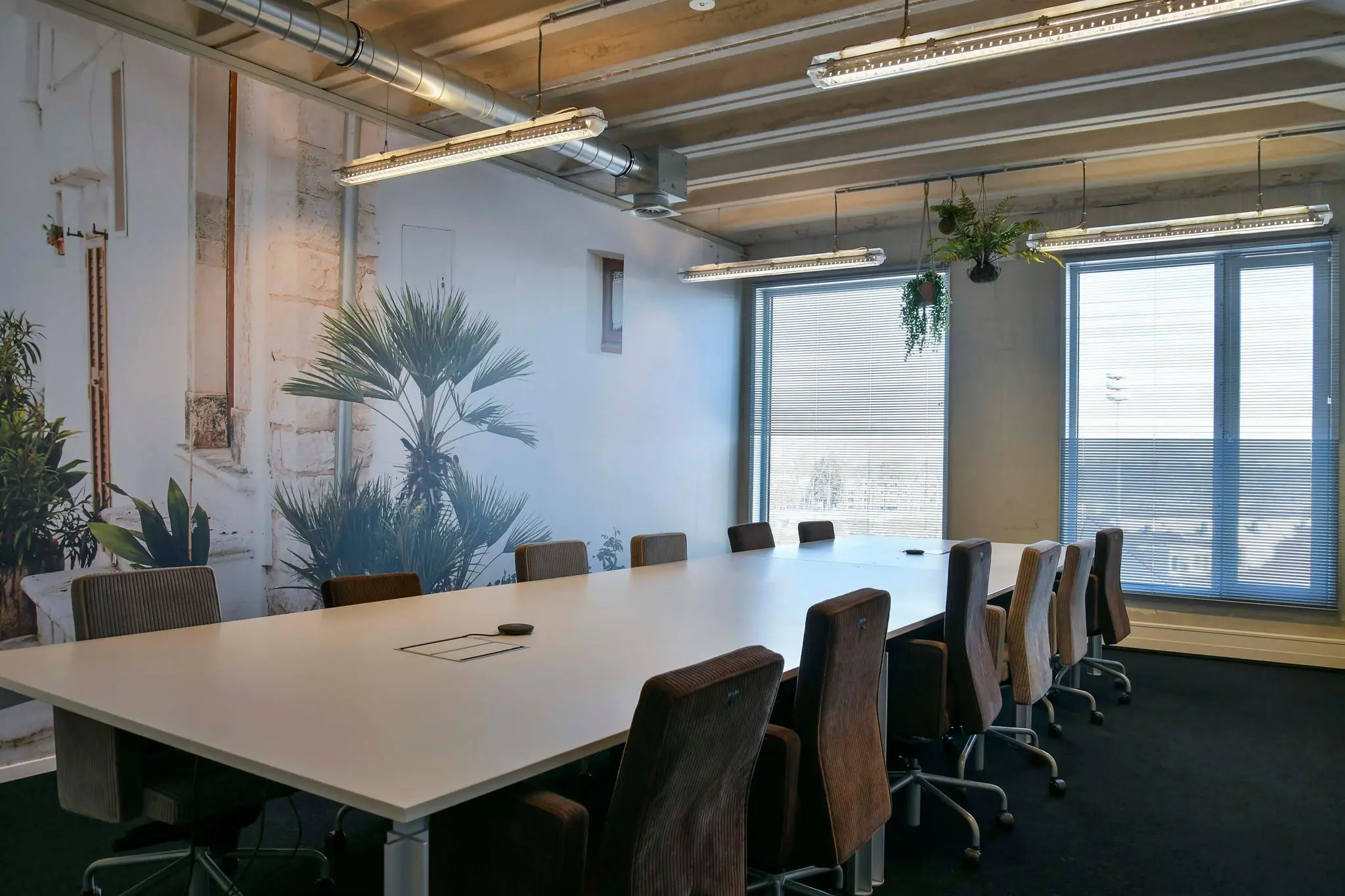 Vergaderruimte aan de Bahialaan met een lange witte tafel, bruine stoelen en een muurdecoratie met tropische planten.