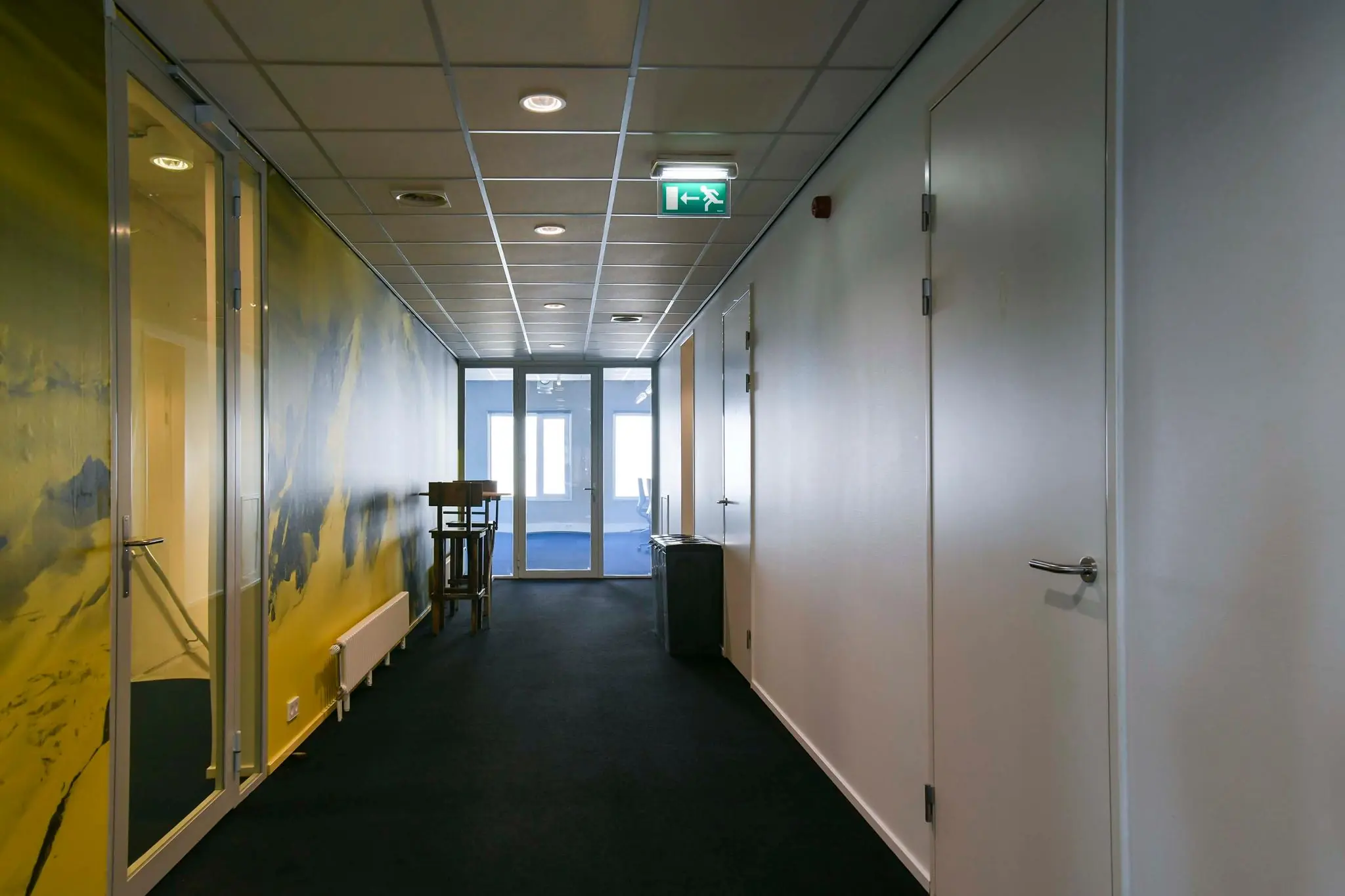 Verlicht kantoorhal met gele muurdecoratie en glazen deur aan het einde op Bahialaan.