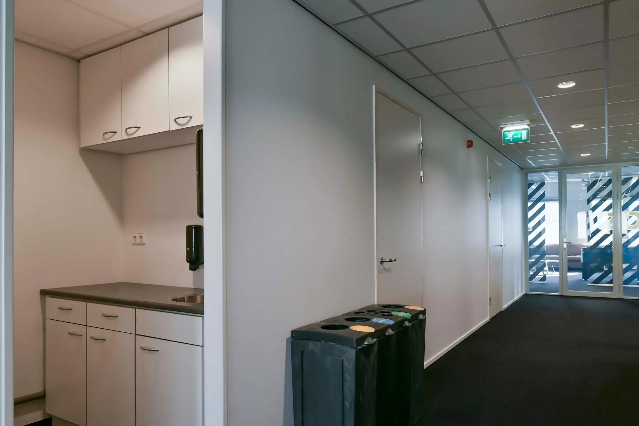 Kantoorhal met kitchenette, afvalscheidingsbakken en glazen deur met decoratieve raamfolie aan de Bahialaan.