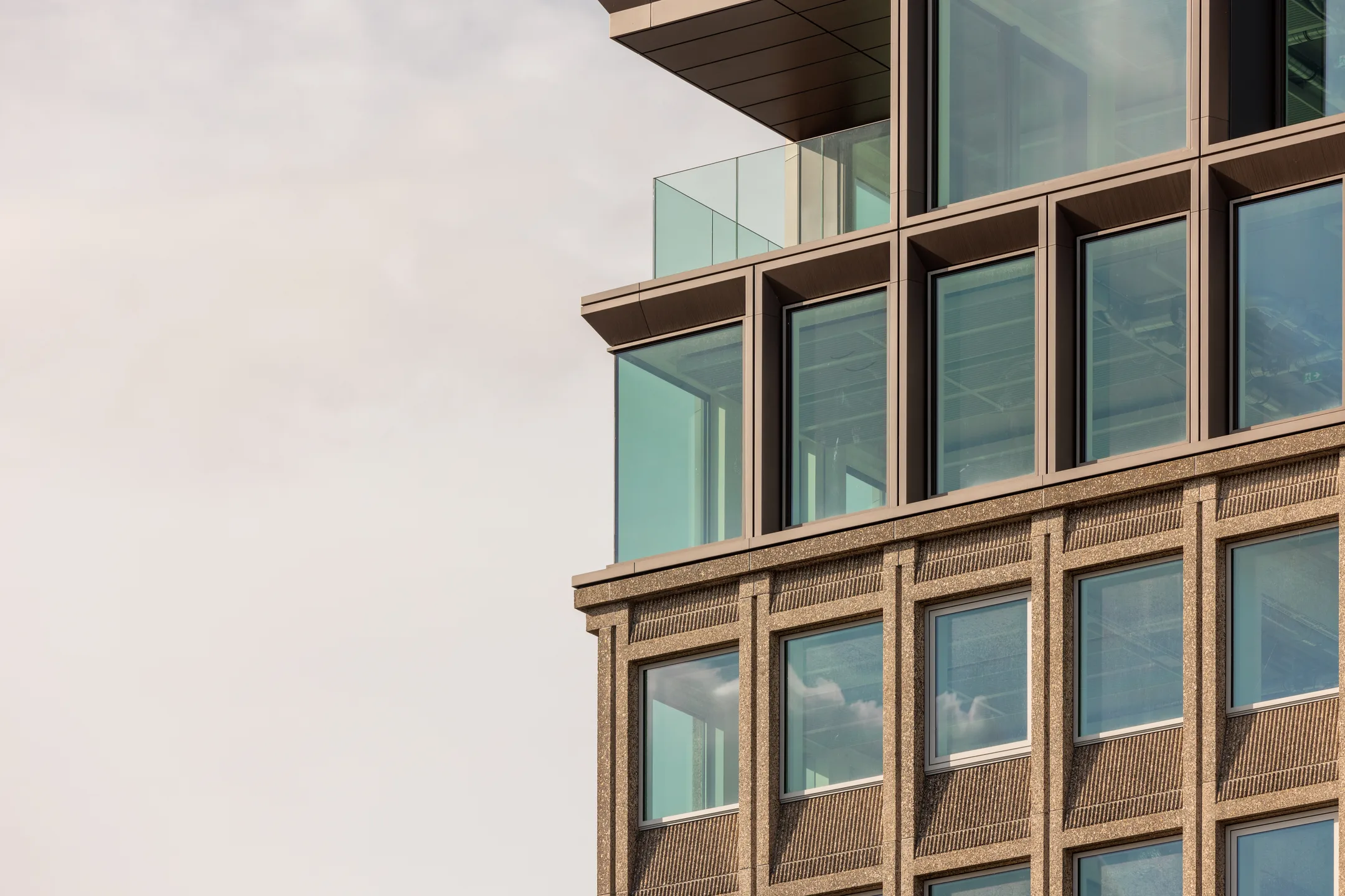 Close-up van een modern gebouw met glas en baksteen, onder een bewolkte lucht.