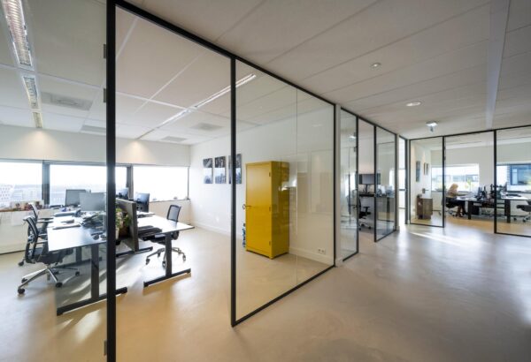 Modern kantoorpand aan het Rietlandpark met glazen wanden, werkplekken en een opvallende gele kast.