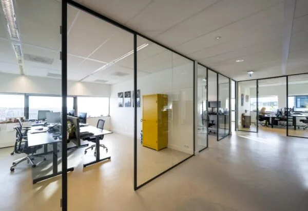 Modern kantoorpand aan het Rietlandpark met glazen wanden, werkplekken en een opvallende gele kast.