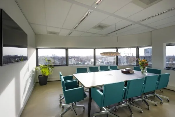 Vergaderruimte in Rietlandpark met turquoise stoelen, uitzicht over de stad en een moderne hanglamp.