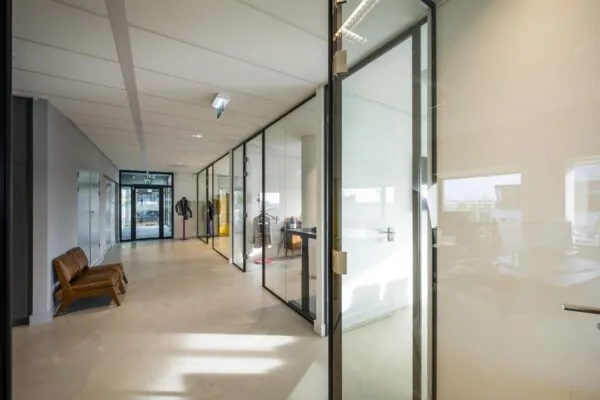 Moderne kantoorhal in Rietlandpark met glazen kantoormuren, minimalistisch interieur en leren bankje.