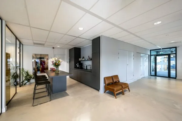 Moderne ontvangst- of kantoorruimte in Rietlandpark met een keukenblok, hoge tafel met barkrukken, zitstoelen en glazen ingang.