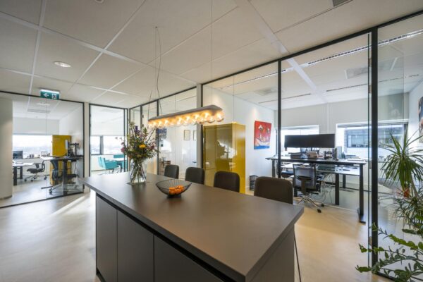 Moderne kantooruimte in Rietlandpark met glazen wanden, een vergadertafel, bloemenvaas en werkplekken.