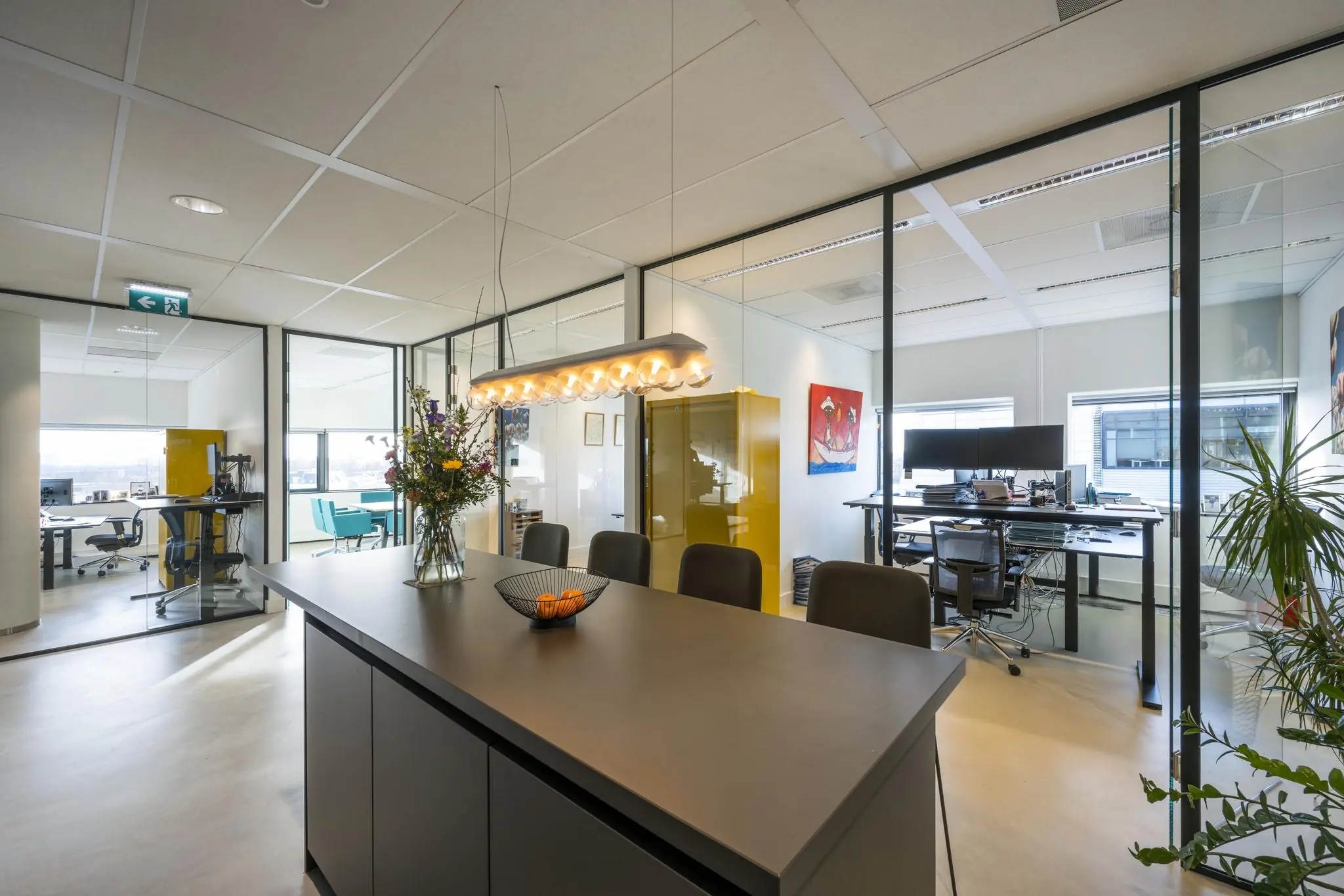 Moderne kantooruimte in Rietlandpark met glazen wanden, een vergadertafel, bloemenvaas en werkplekken.