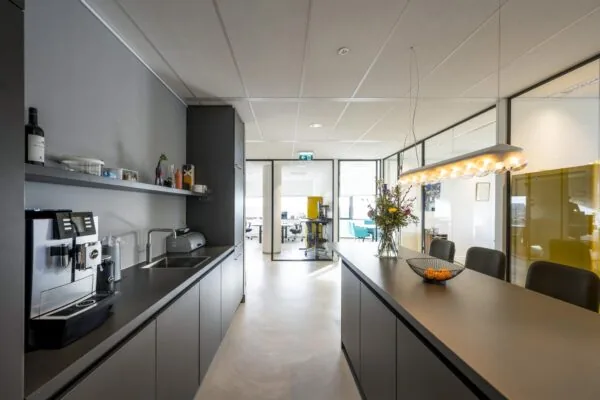 Moderne kantoorkeuken bij Rietlandpark met een koffiezetapparaat, bar, bloemenvaas en uitzicht op vergaderruimtes.