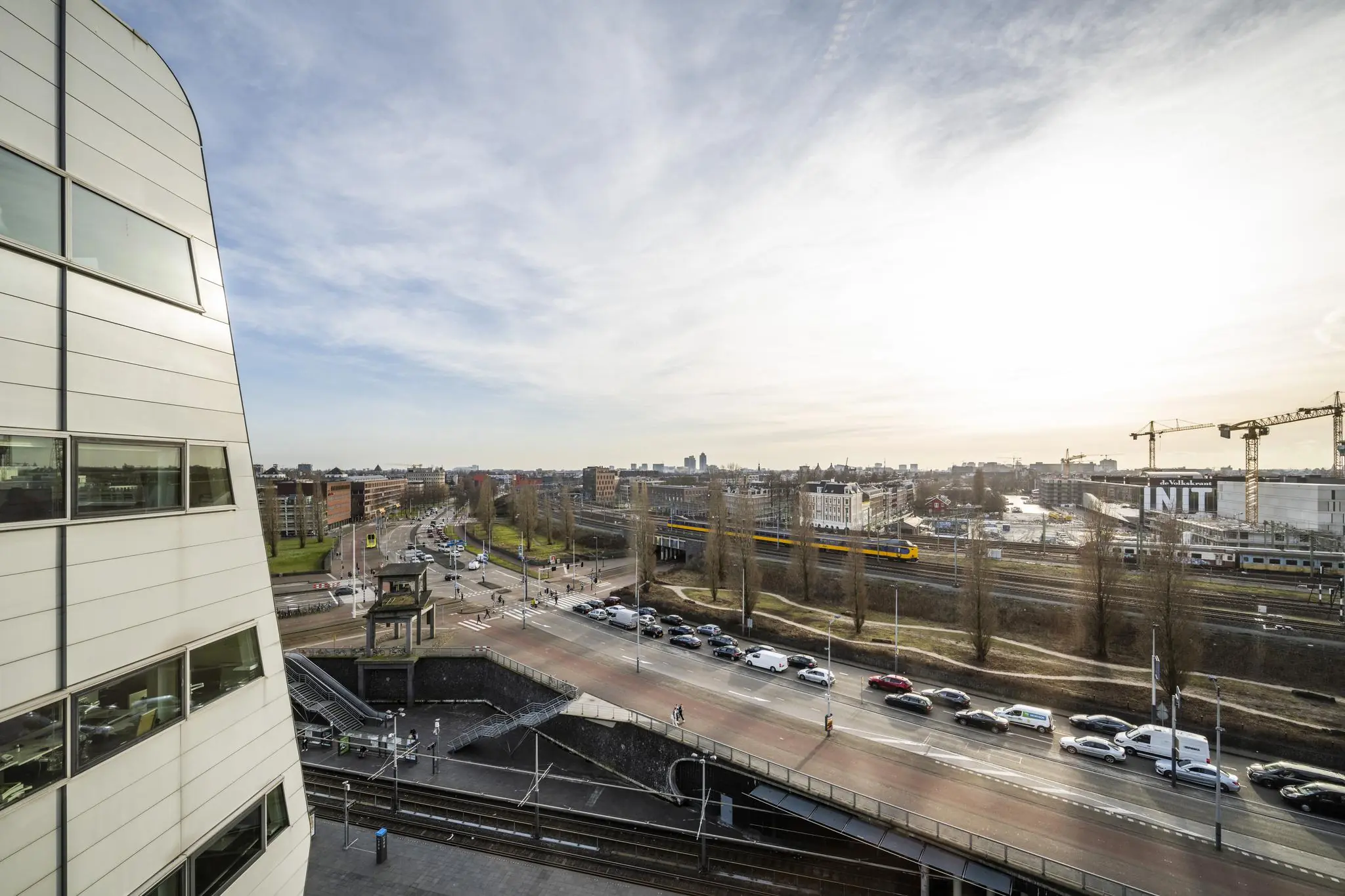 Luchtfoto van Rietlandpark in Amsterdam met druk verkeer, treinspoor en moderne gebouwen bij zonsondergang.