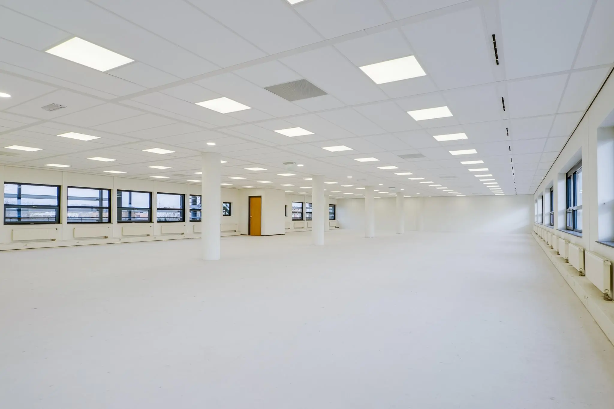 Lege, lichte kantoorruimte aan de Marconibaan met witte vloeren, ramen rondom en systeemplafondverlichting.