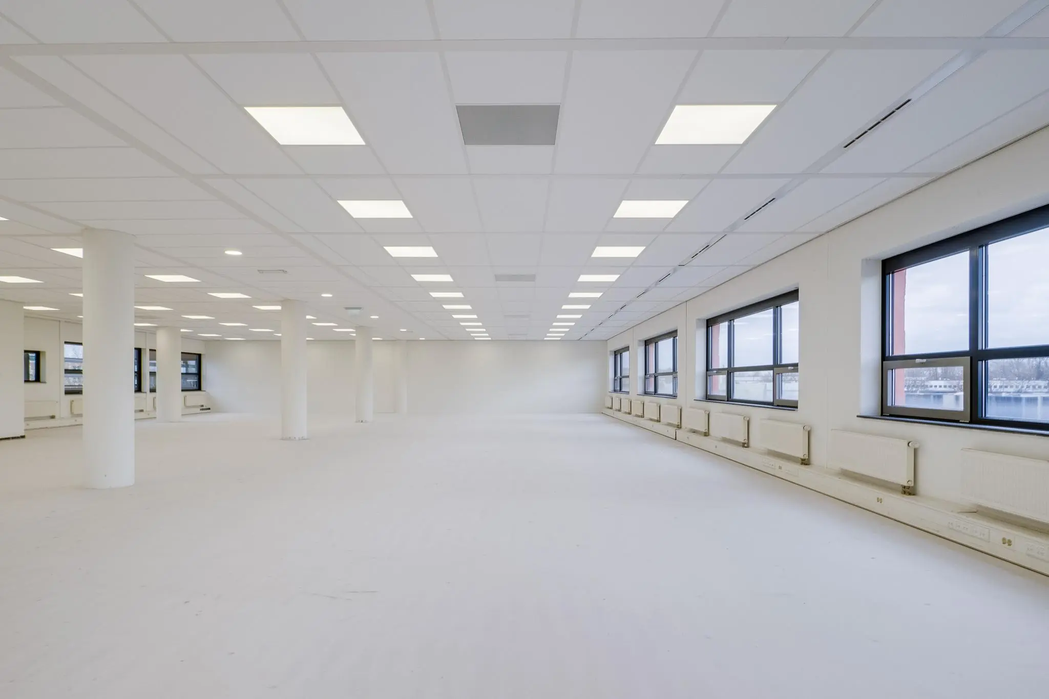 Licht en ruim leeg kantoorinterieur aan de Marconibaan met witte wanden, plafondverlichting en grote ramen.