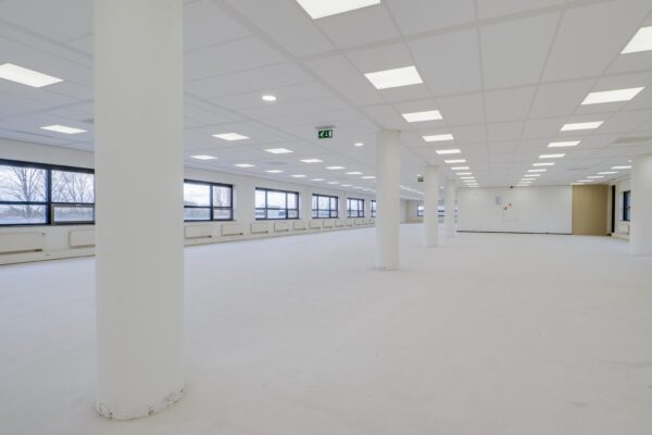 Een grote, lege en licht verlichte kantoorruimte aan de Marconibaan met witte wanden, plafond en vloer.