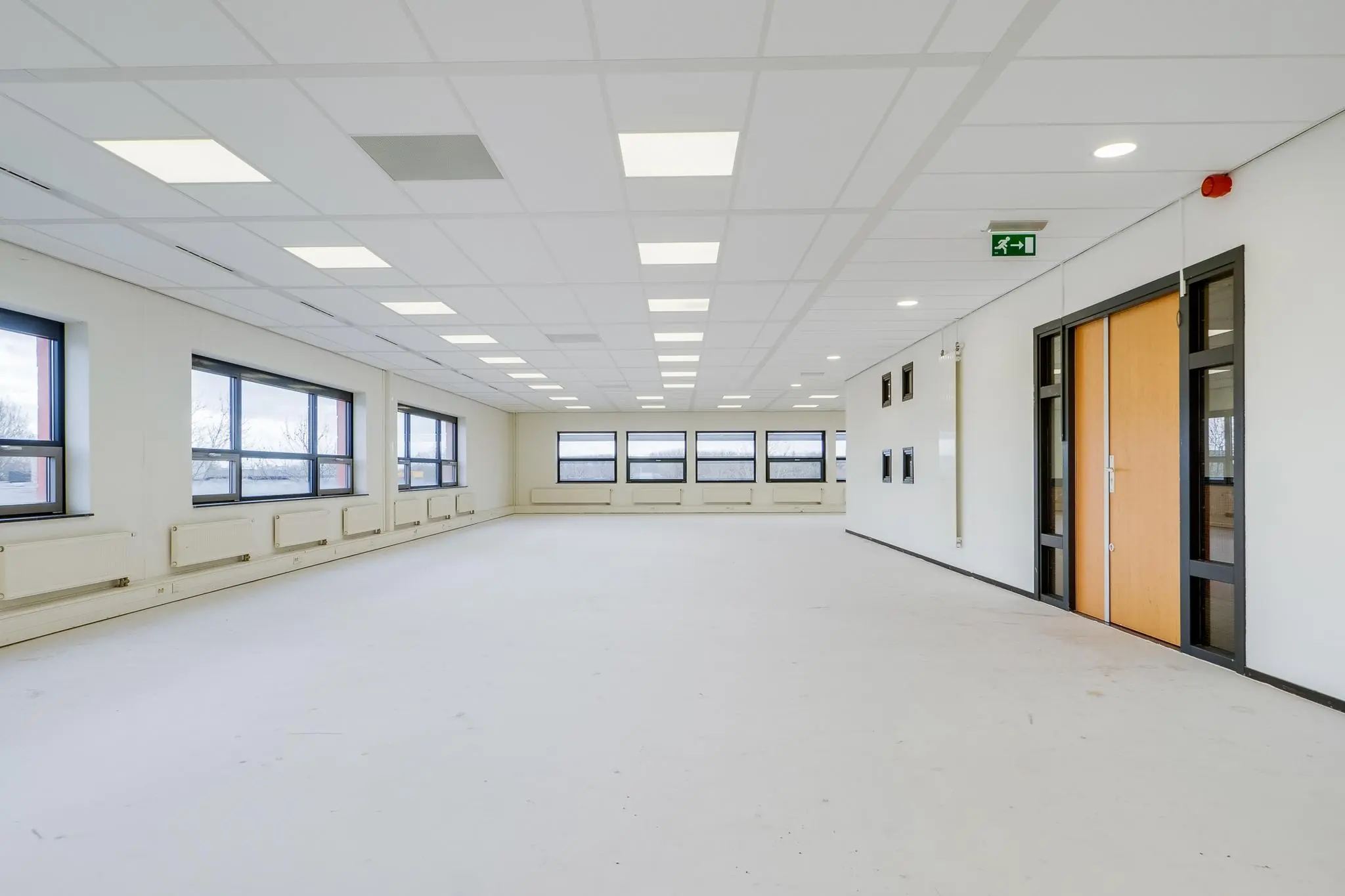 Lege, lichte kantoorruimte aan de Marconibaan met grote ramen en systeemplafond.