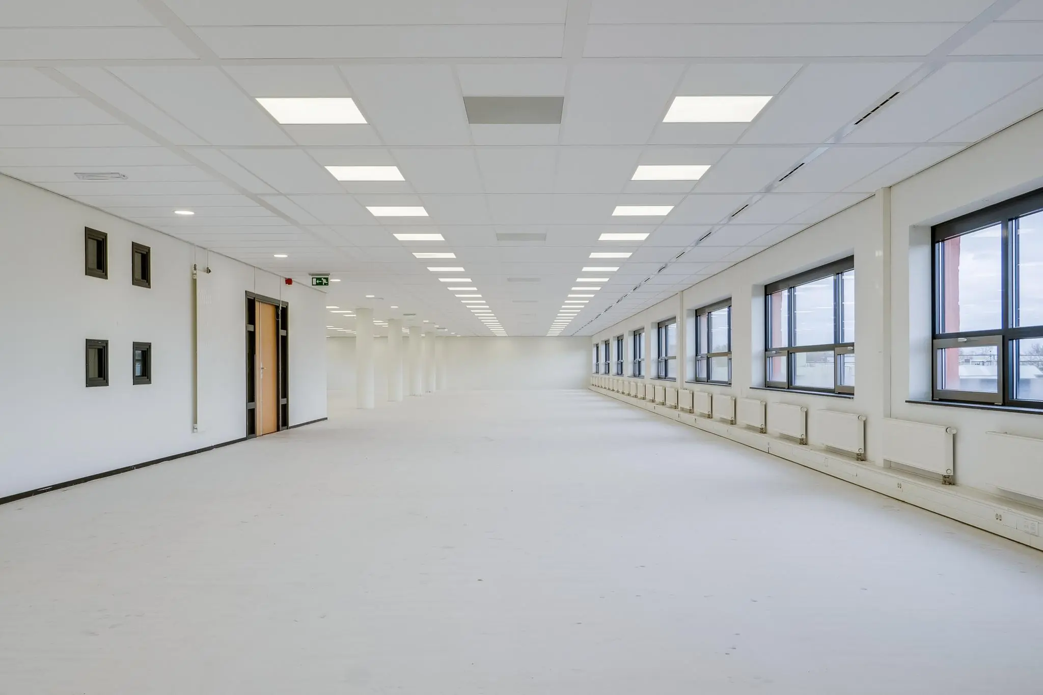 Lege, ruime kantoorruimte aan de Marconibaan met systeemplafond en grote ramen aan één zijde.