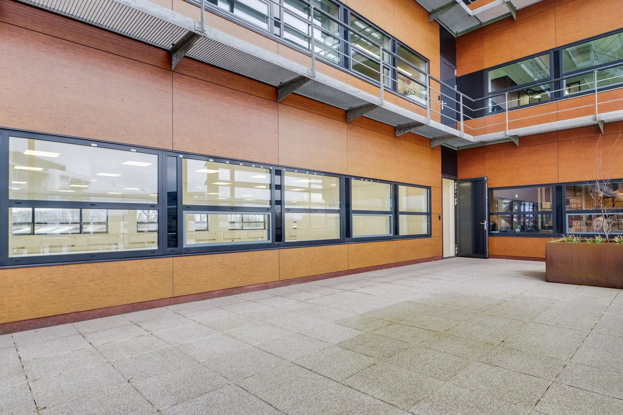 Binnenplaats van een modern kantoorgebouw aan de Marconibaan met houten gevelpanelen, grote ramen en een open deur.