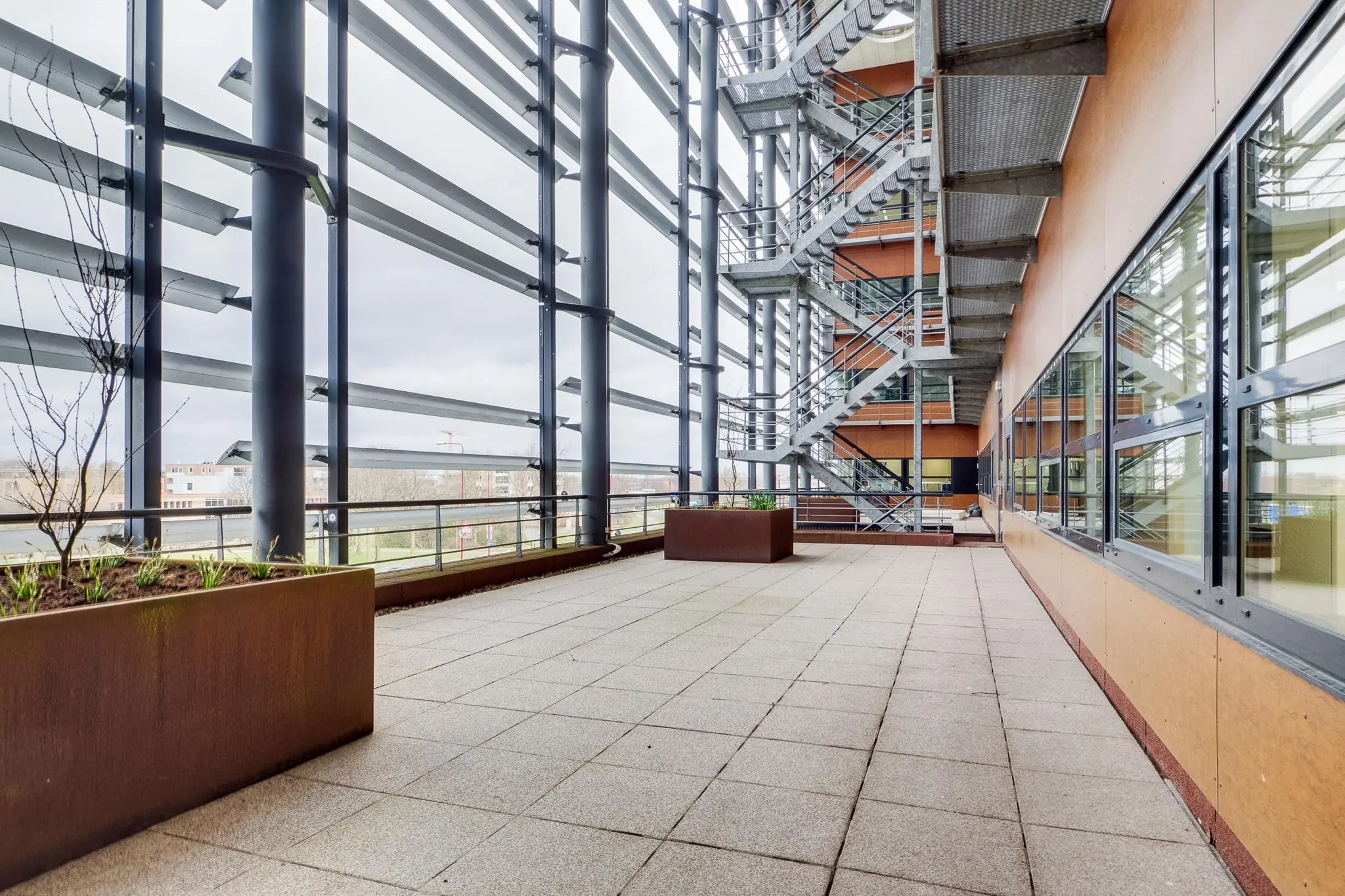 Ruim betegeld dakterras met plantenbakken en metalen buitentrap aan het Marconibaan-gebouw.