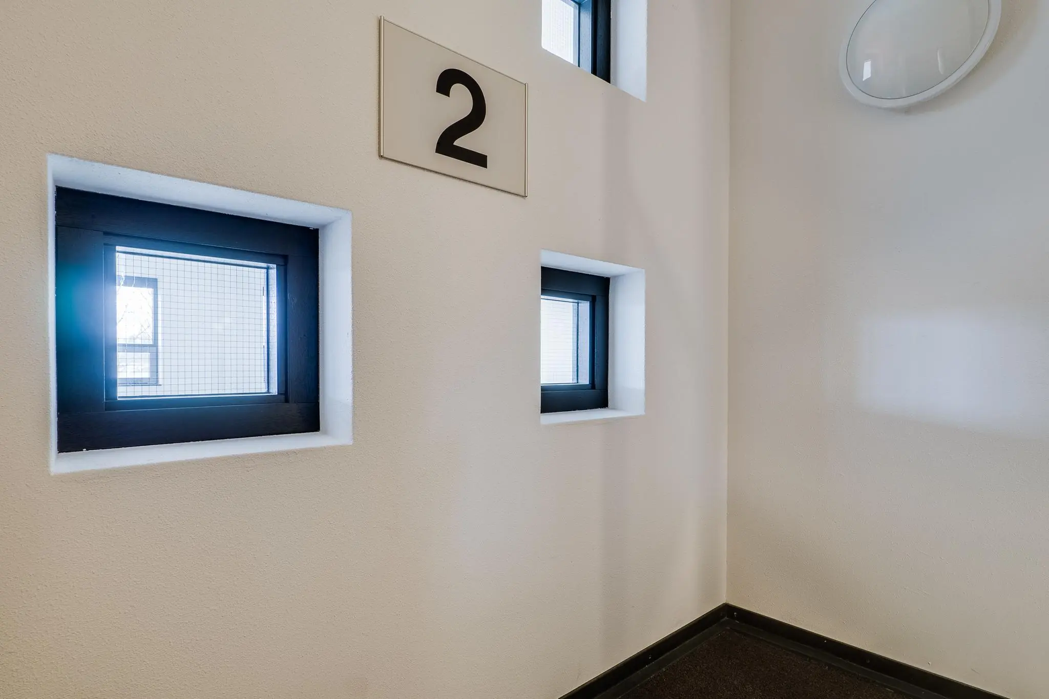 Witte muur met vier kleine ramen en een bord met het cijfer 2 in een trappenhuis aan de Marconibaan.