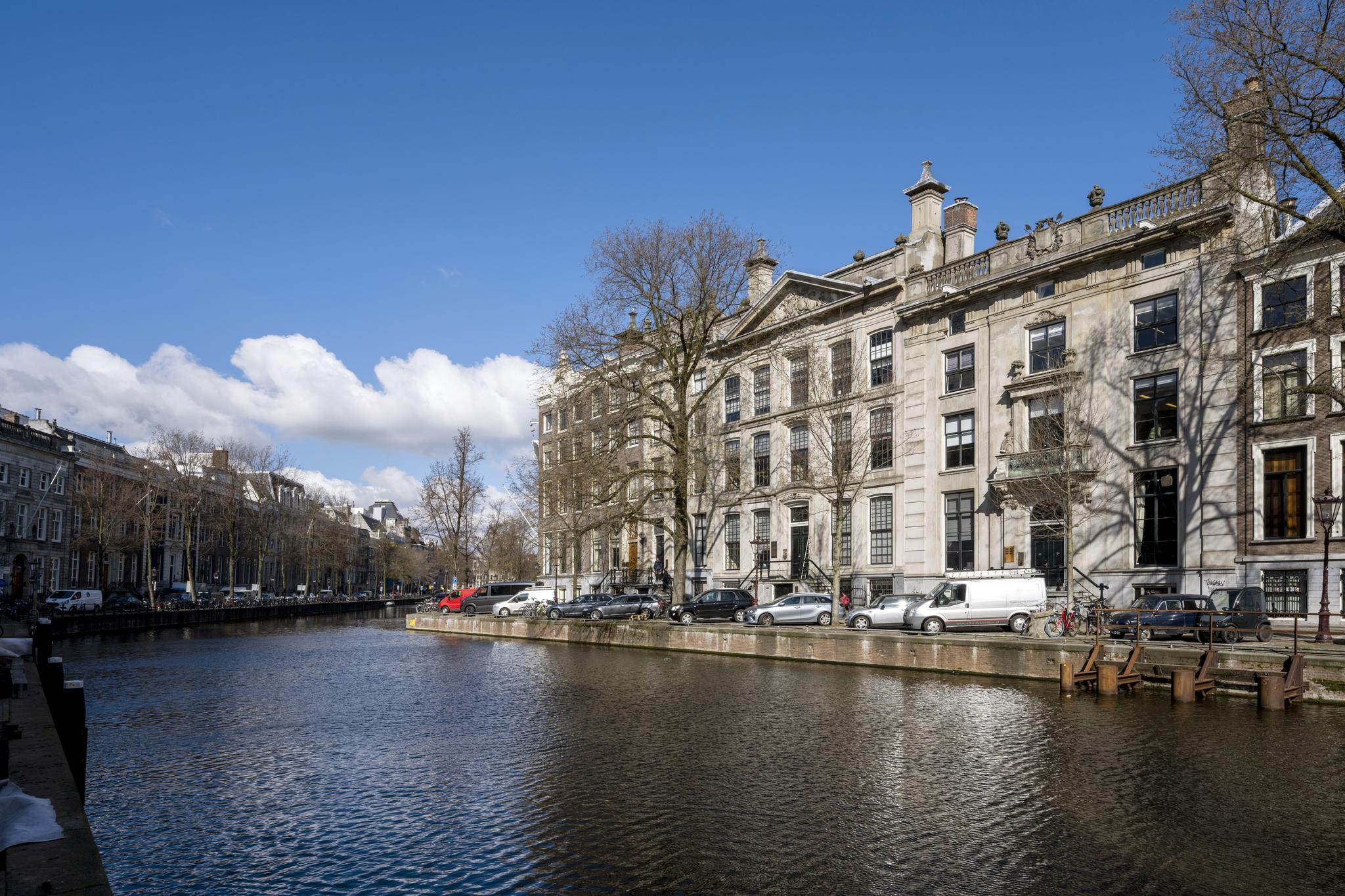 Monumentale grachtenpanden aan de Herengracht in Amsterdam met een heldere blauwe lucht en zicht op het water.