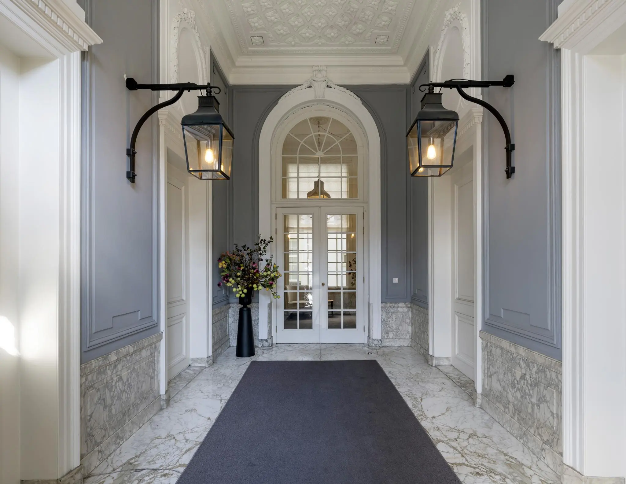 Elegante entreehal aan de Herengracht met marmeren vloer, grijze wandpanelen en klassieke dubbele deuren.