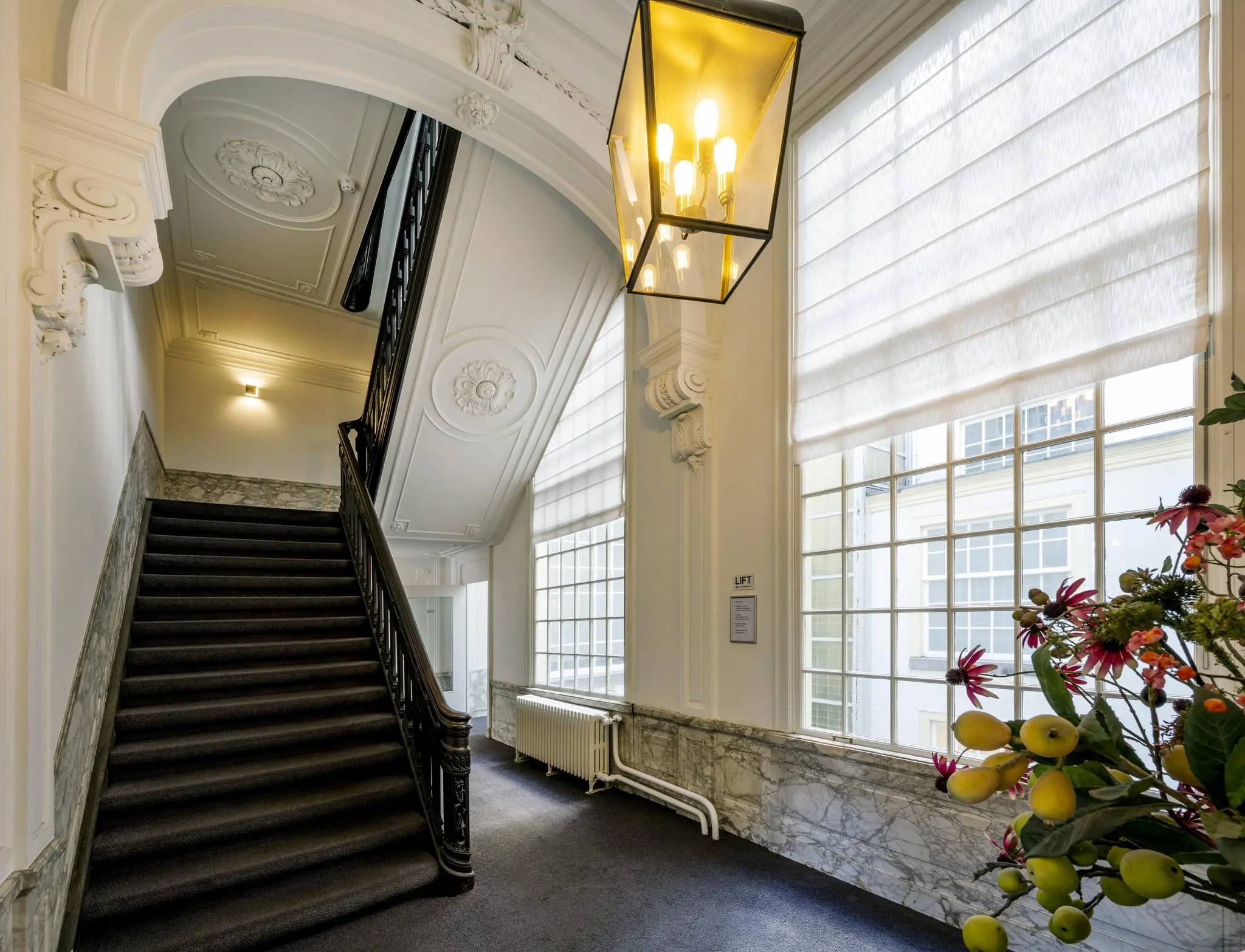 Trapportaal met sierlijk plafond, grote ramen en een klassieke lantaarn in een pand aan de Herengracht.