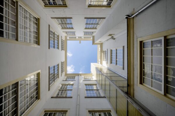 Blik omhoog vanuit een binnenplaats naar de blauwe lucht tussen de hoge witte gevels van Herengracht 103-703 in Amsterdam.
