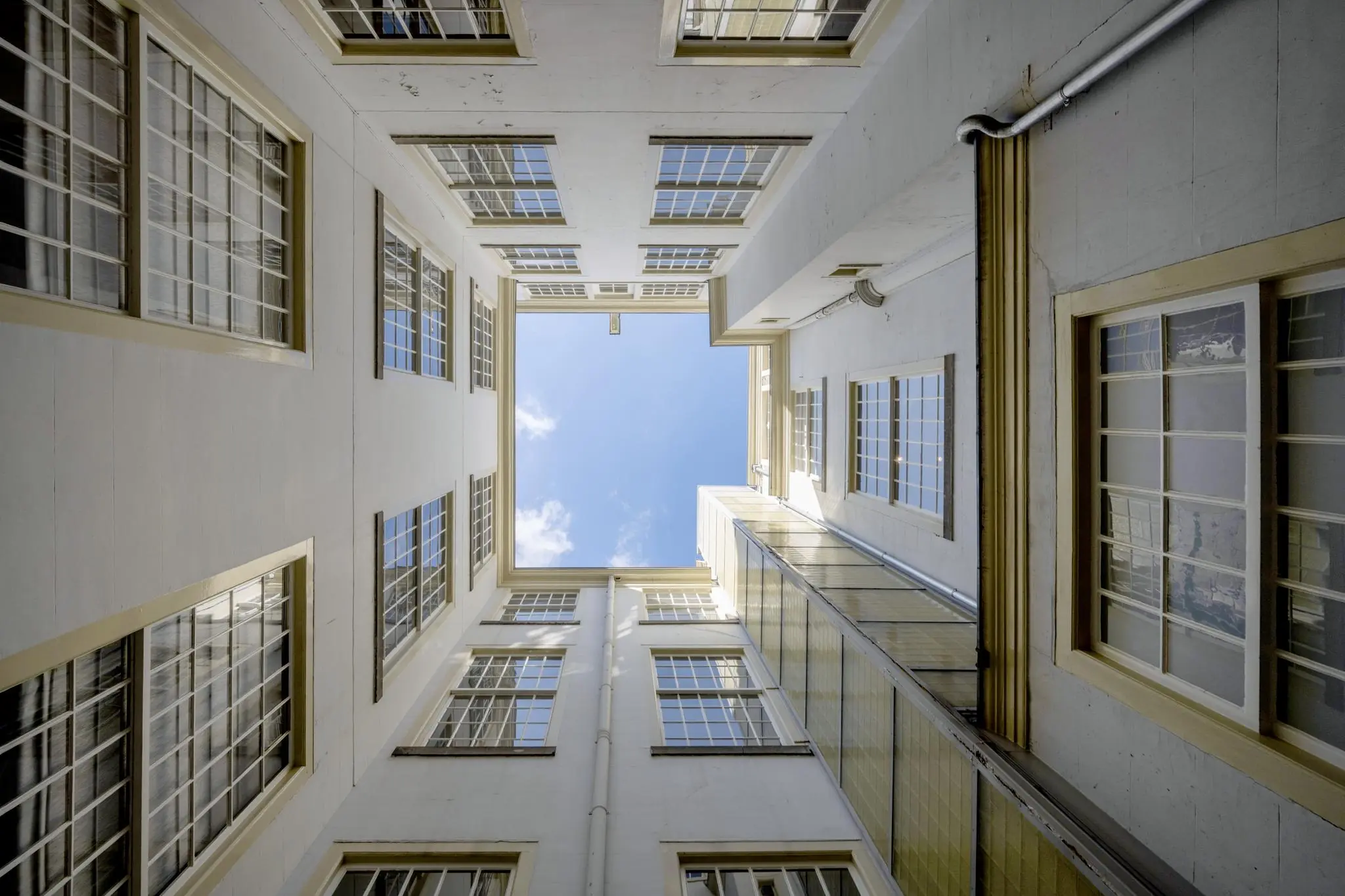 Blik omhoog vanuit een binnenplaats naar de blauwe lucht tussen de hoge witte gevels van Herengracht 103-703 in Amsterdam.