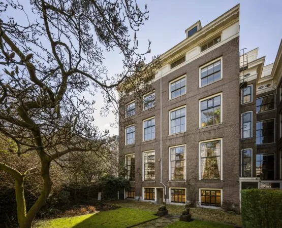 Achterzijde van een klassiek grachtenpand aan de Herengracht met grote ramen en een groene stadstuin.