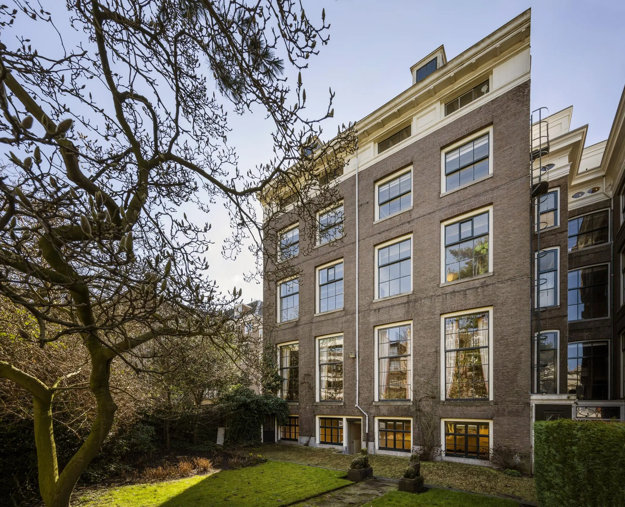 Achterzijde van een klassiek grachtenpand aan de Herengracht met grote ramen en een groene stadstuin.