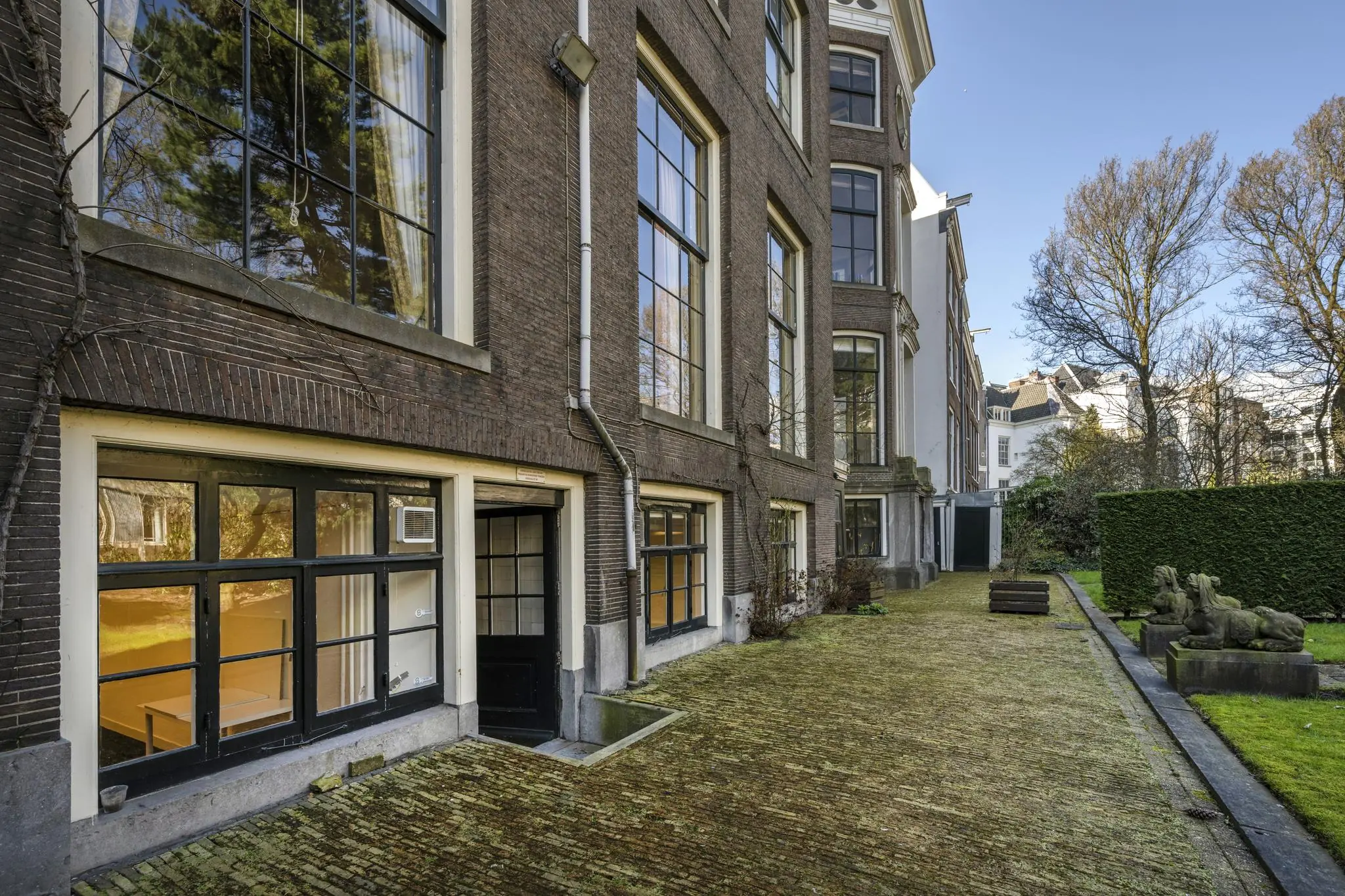 Achterzijde van een grachtenpand aan de Herengracht met grote ramen, een binnentuin en twee beelden van liggende leeuwen.