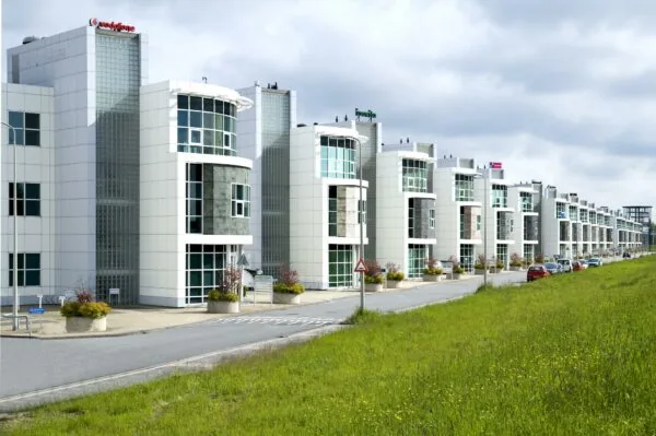 Rij moderne kantoorgebouwen aan het Rhijnspoor met glazen gevels en bedrijfslogo’s, gezien vanaf een grasstrook langs de weg.