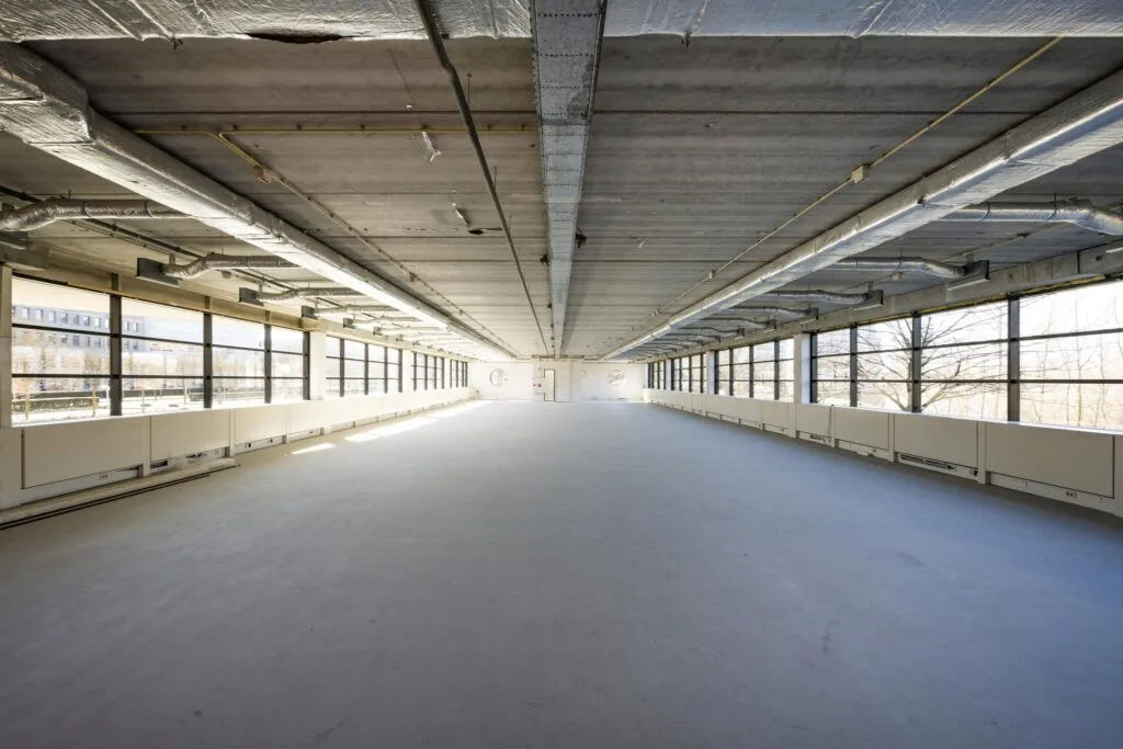Leeg en licht industrieel kantoorpand aan de Wegalaan met grote ramen en zichtbare plafondleidingen.